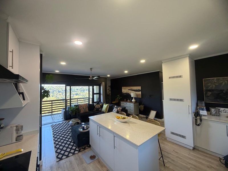 Modern open-plan living area featuring a central kitchen island with quartz countertops, recessed lighting, and seamless flow to a balcony with scenic views.