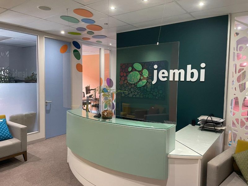 A professional office reception area featuring a custom curved desk, glass partitions, and modern acoustic ceiling detailing with a branded feature wall.