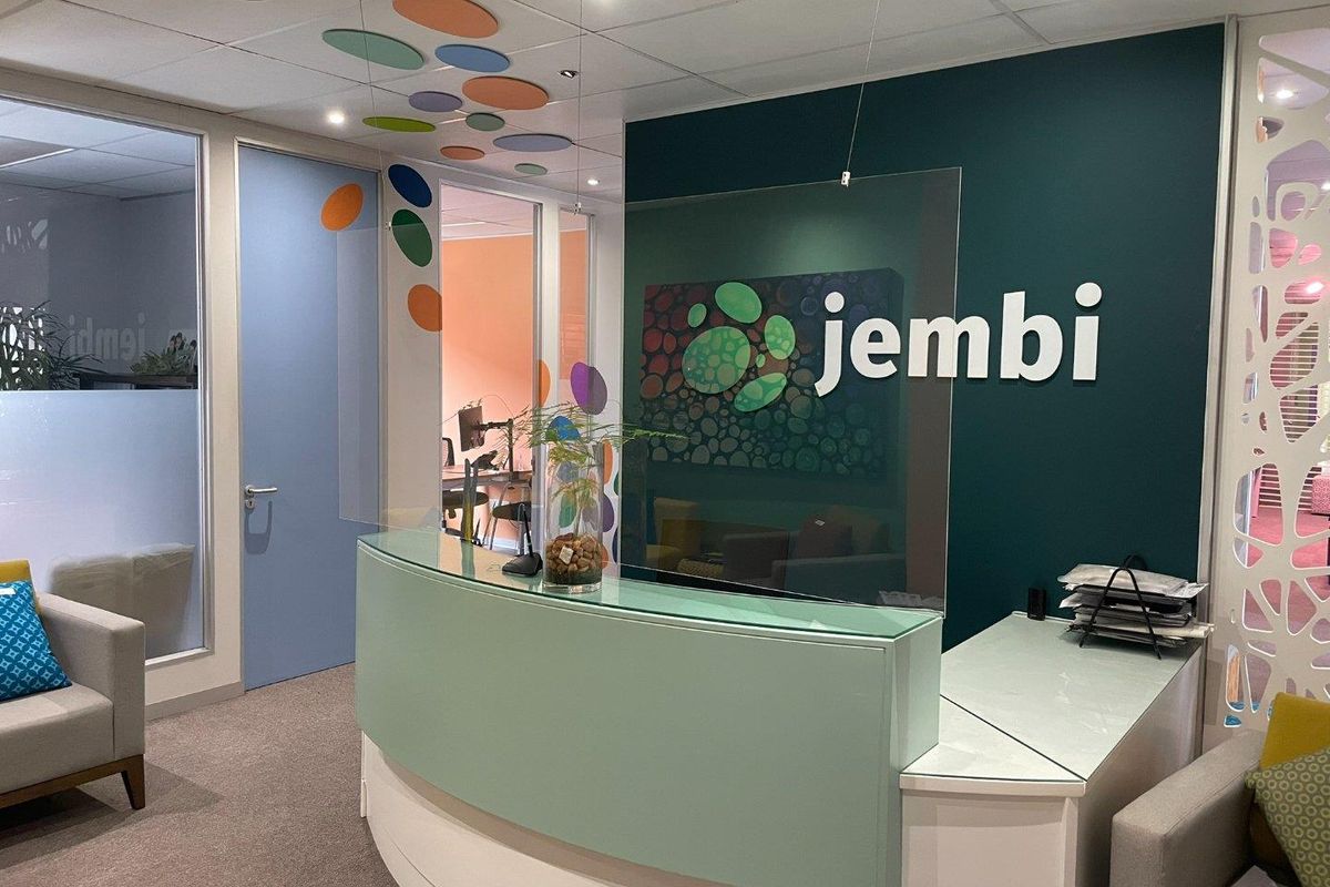 A professional office reception area featuring a custom curved desk, glass partitions, and modern acoustic ceiling detailing with a branded feature wall.
