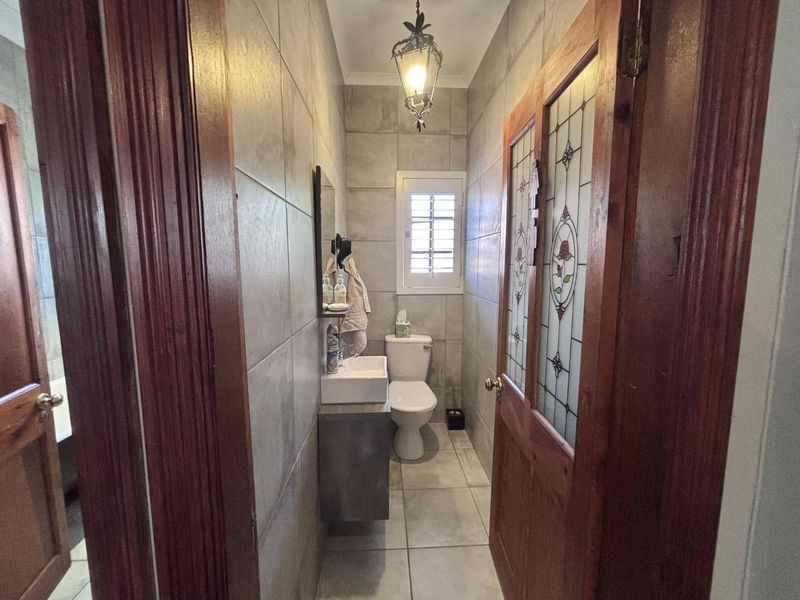 A compact bathroom featuring full-height wall tiling, a wall-mounted vanity with basin, a toilet, and a decorative stained glass door.