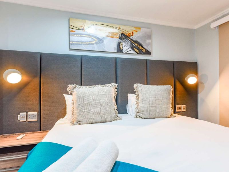 A well-maintained bedroom featuring a modern upholstered headboard, integrated wall-mounted reading lights, and convenient built-in bedside shelving with electrical access.