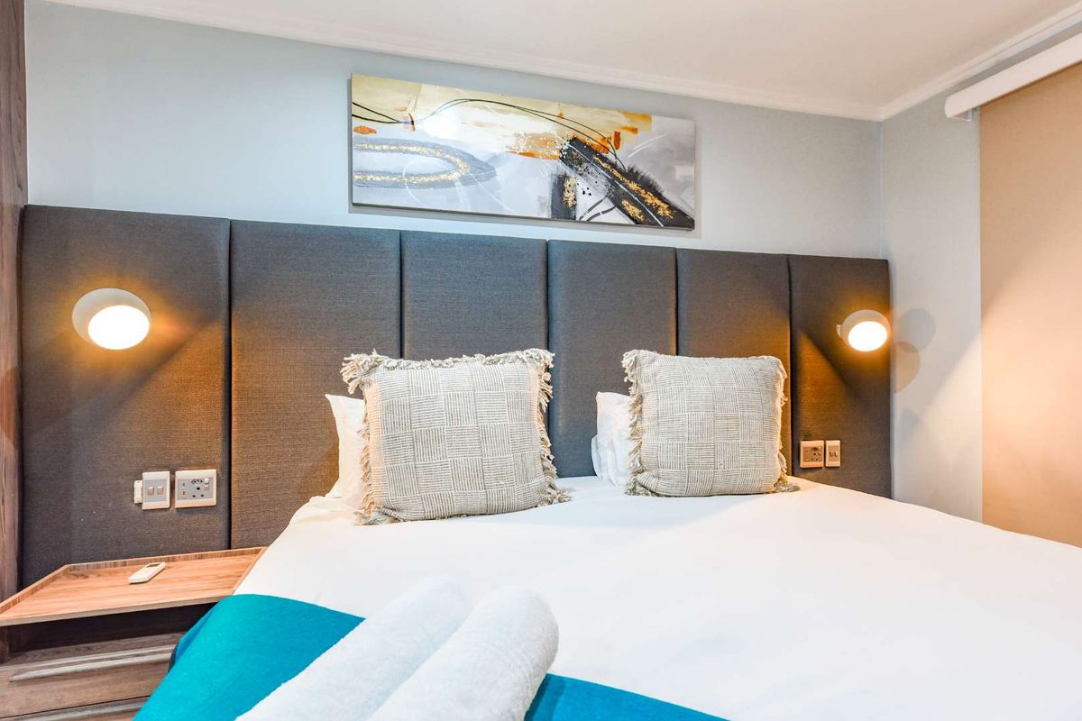 A well-maintained bedroom featuring a modern upholstered headboard, integrated wall-mounted reading lights, and convenient built-in bedside shelving with electrical access.