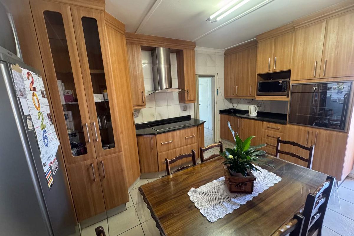 A functional kitchen featuring wood-veneer cabinetry, black granite countertops, a built-in oven, and a stainless steel extractor fan, with an integrated dining area.