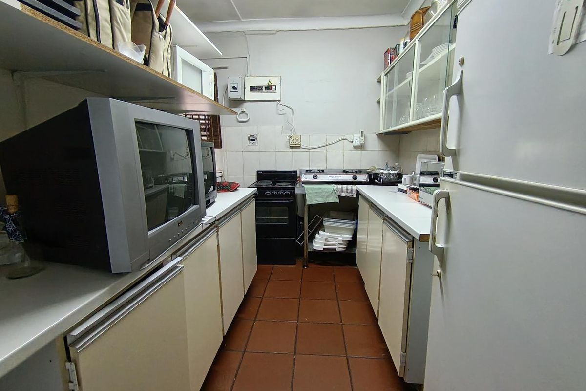 A compact, dated kitchen featuring tiled flooring, built-in cabinetry, and a functional layout with integrated stove and cooktop.