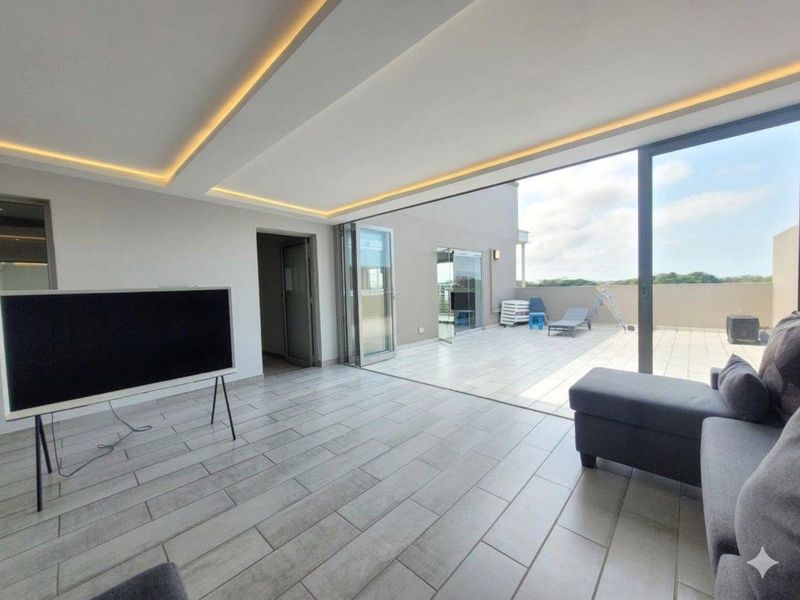 Modern open-plan living area featuring recessed ceiling lighting, large format tiled flooring, and seamless stacking glass doors opening onto a spacious balcony.