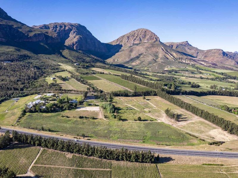 An expansive aerial view of a large farm property featuring vast vineyards, open agricultural land, and a scenic mountain backdrop.
