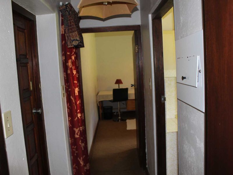 A narrow interior hallway featuring timber door frames and access to adjacent rooms, showing signs of wear and dated finishes.