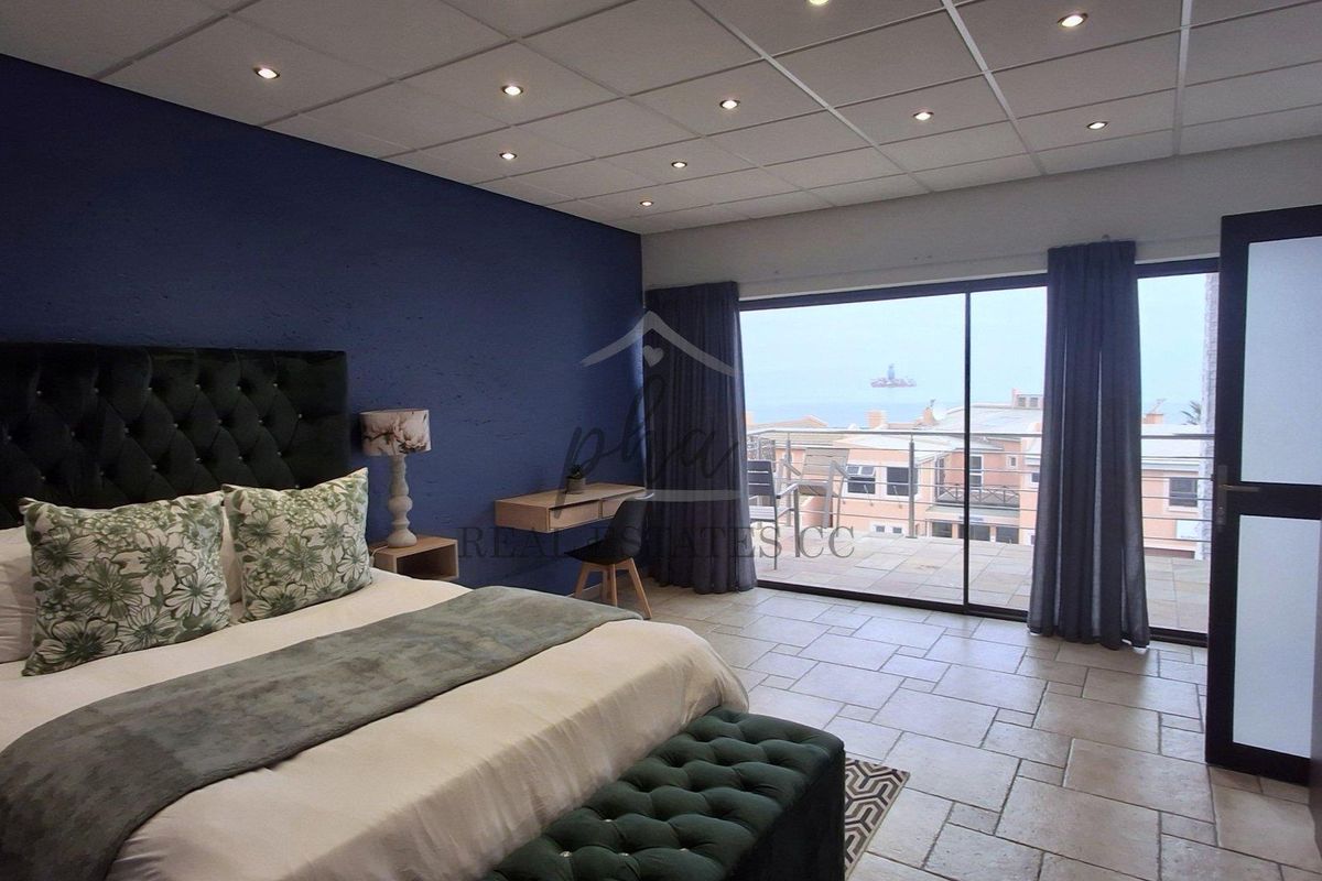 Spacious bedroom featuring tiled flooring, recessed ceiling lights, and large sliding glass doors opening onto a balcony with coastal views.