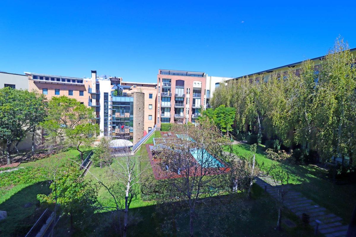 Elevated view overlooking the apartment complex courtyard, featuring landscaped gardens, mature trees, and a central swimming pool area.