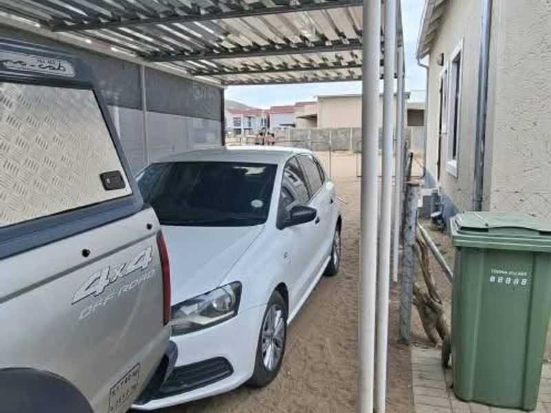 A covered carport area with a corrugated metal roof and paved flooring, providing sheltered parking space alongside the property.