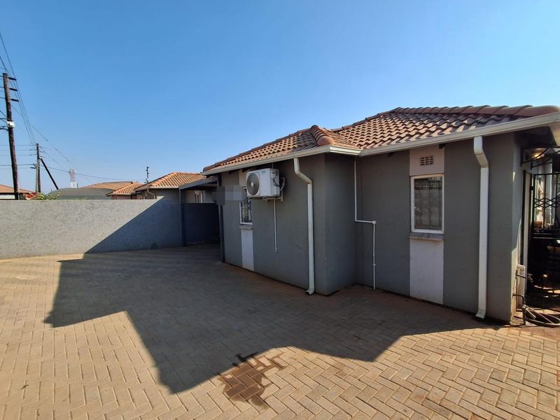 Rear exterior view of the property featuring a paved driveway, tiled roof, and mounted air conditioning unit.