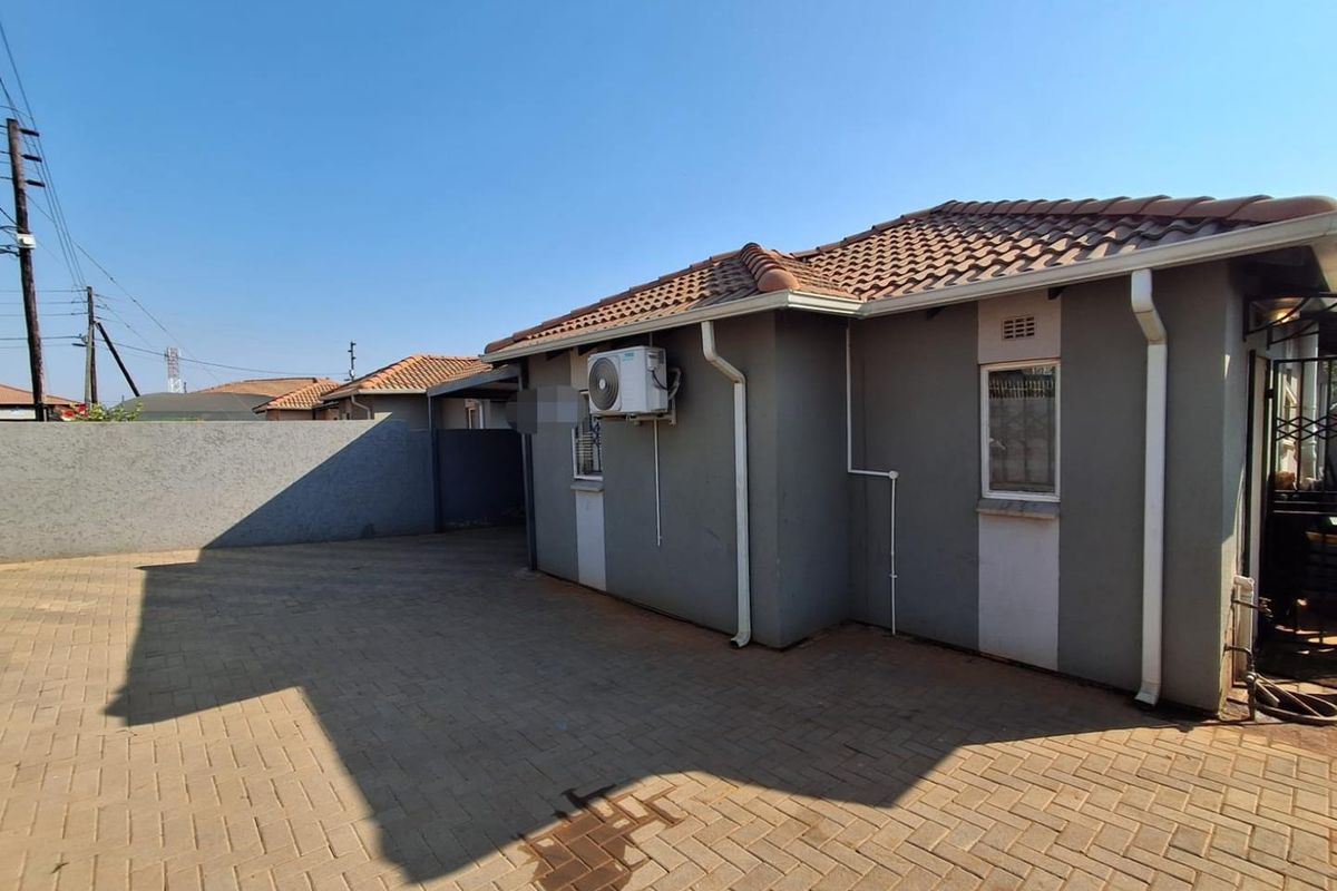 Rear exterior view of the property featuring a paved driveway, tiled roof, and mounted air conditioning unit.