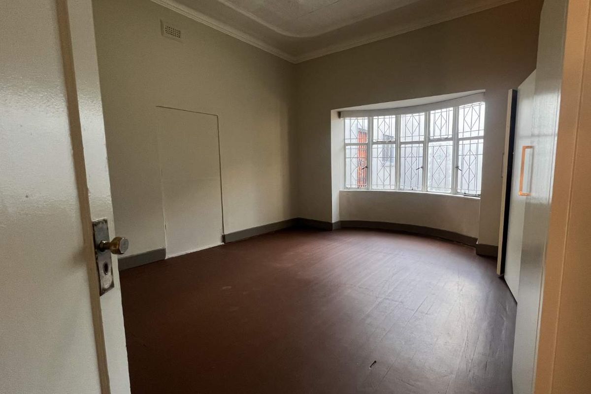 An empty bedroom featuring a classic bay window, decorative ceiling rose, ornate cornice, and original timber flooring, offering a blank canvas for renovation.