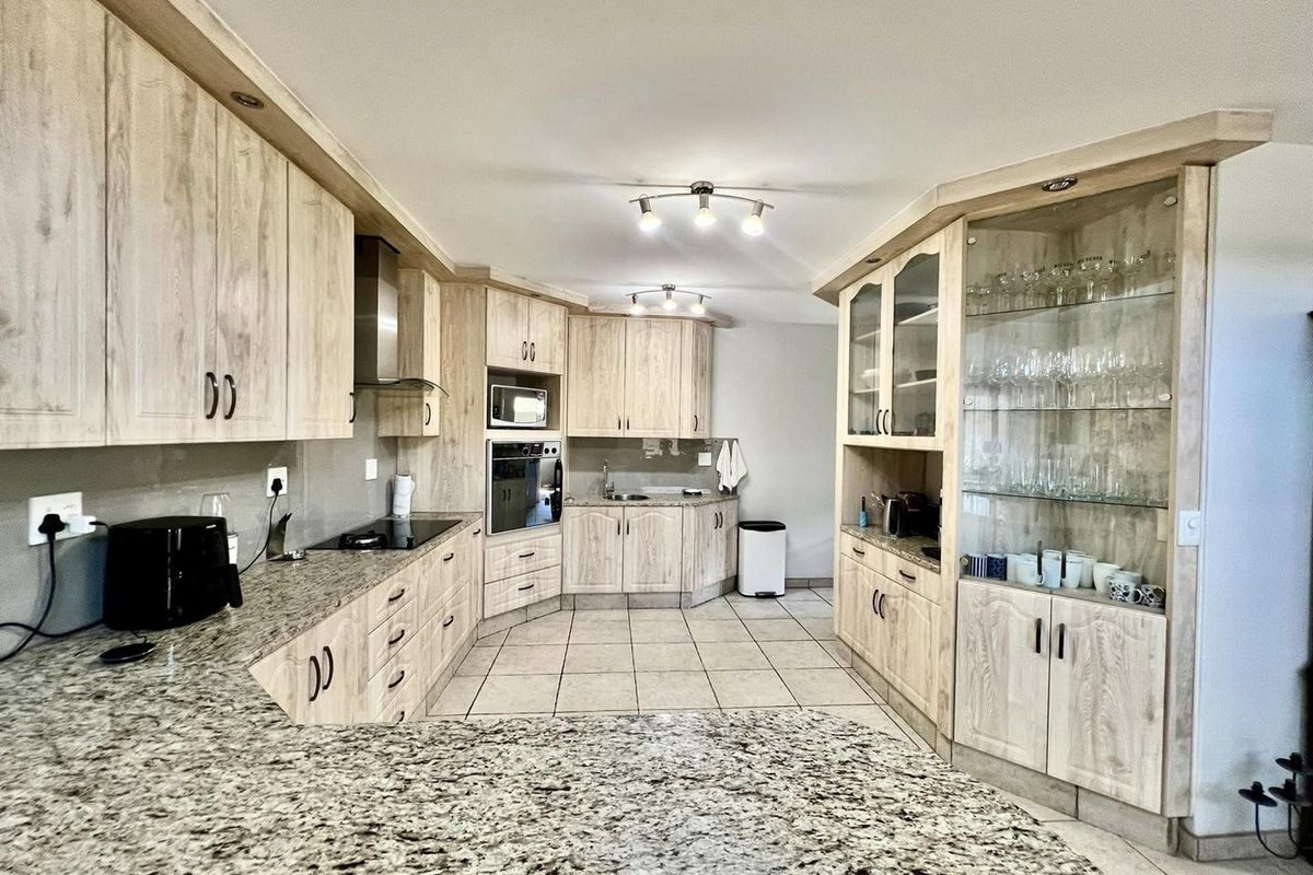 Spacious kitchen featuring light wood-grain cabinetry, granite countertops, integrated oven, and a built-in glass display cabinet, complemented by neutral floor tiling.