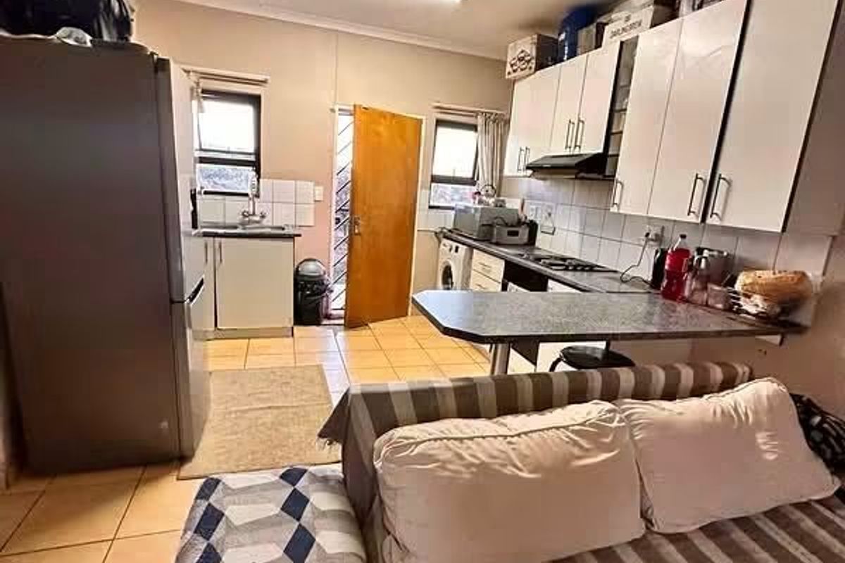 Open-plan kitchen and living area featuring built-in cabinetry, a breakfast bar, and tiled flooring with direct access to an exterior door.