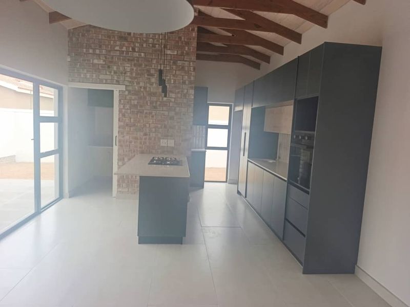 Modern open-plan kitchen featuring dark cabinetry, a central island with a gas hob, exposed brickwork, and high vaulted ceilings with timber rafters.
