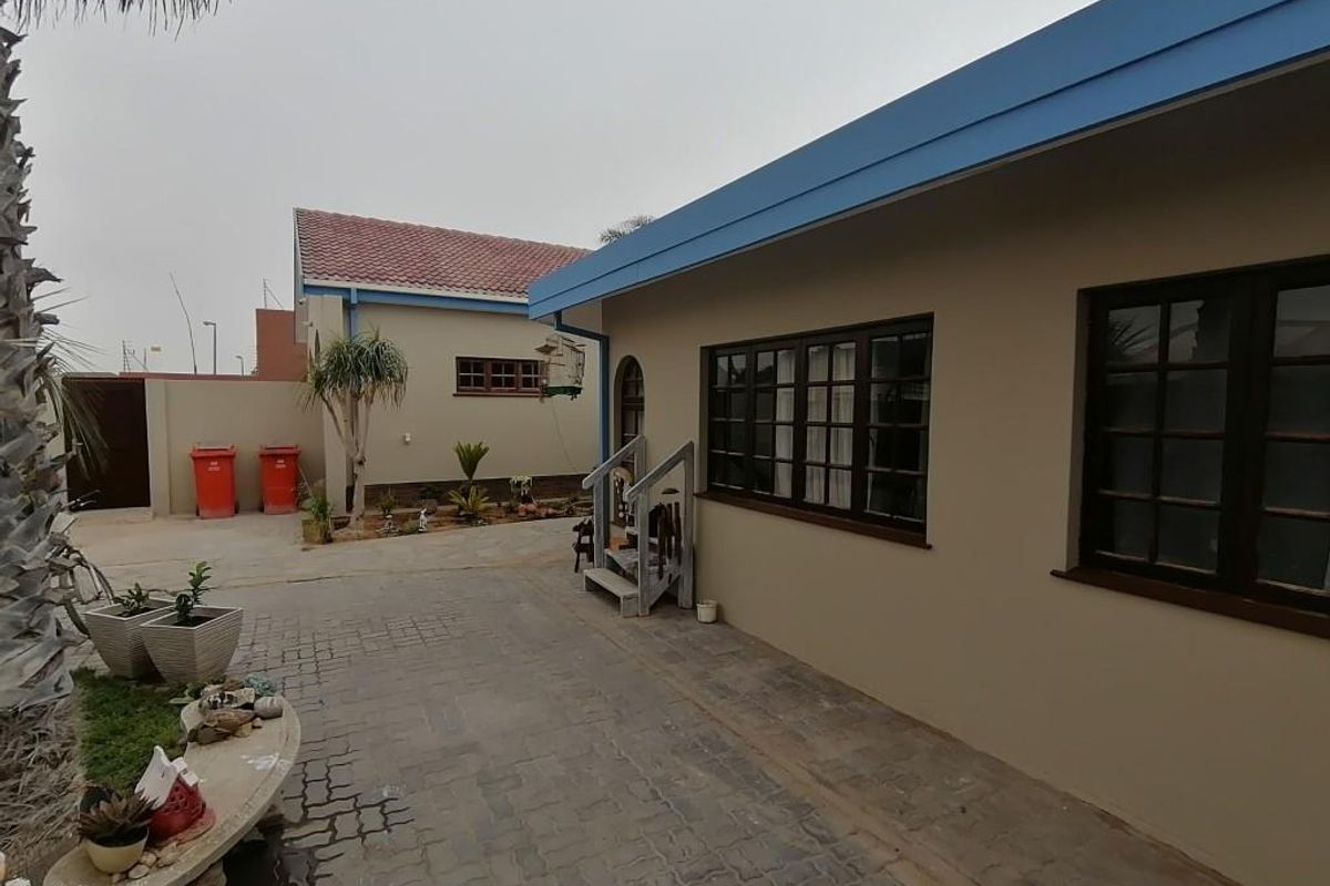 A view of the exterior rear courtyard featuring paved surfaces, a small set of wooden steps, and access to the main building structure.