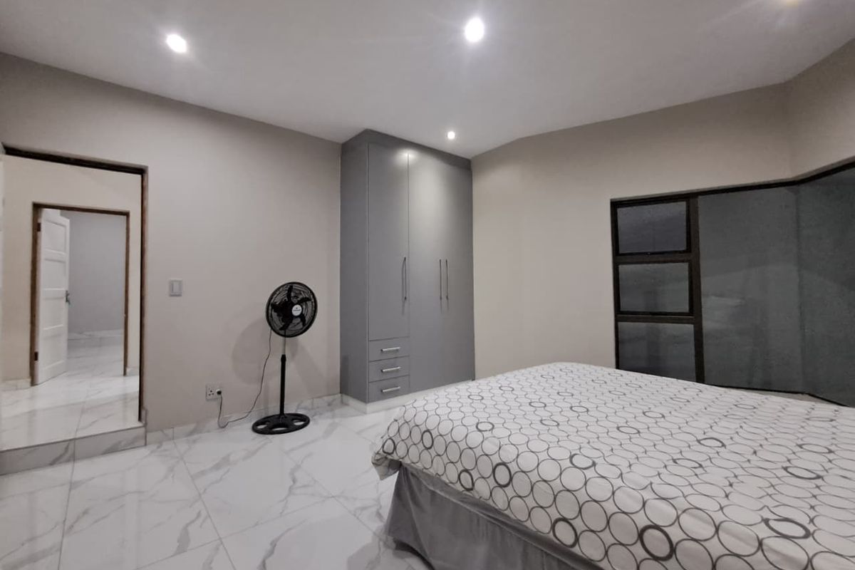 A modern bedroom featuring sleek grey built-in cupboards, polished marble-look floor tiles, and recessed downlighting.