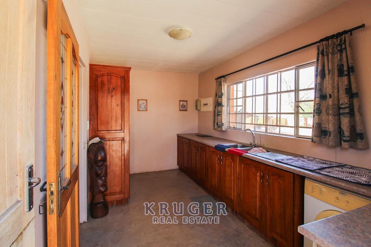 A functional kitchen featuring wooden cabinetry, laminate countertops, and a stainless steel sink, offering a dated aesthetic with potential for modernization.