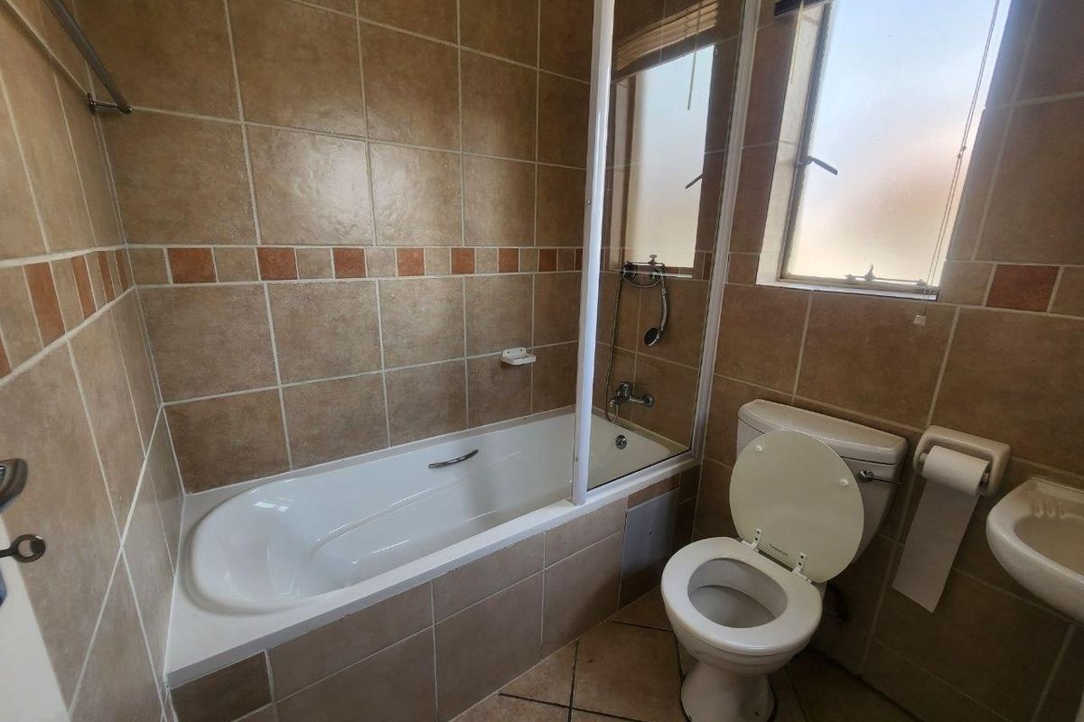 A functional bathroom featuring a bathtub with a shower screen, a toilet, and a wall-mounted basin, finished with neutral-toned wall and floor tiles.