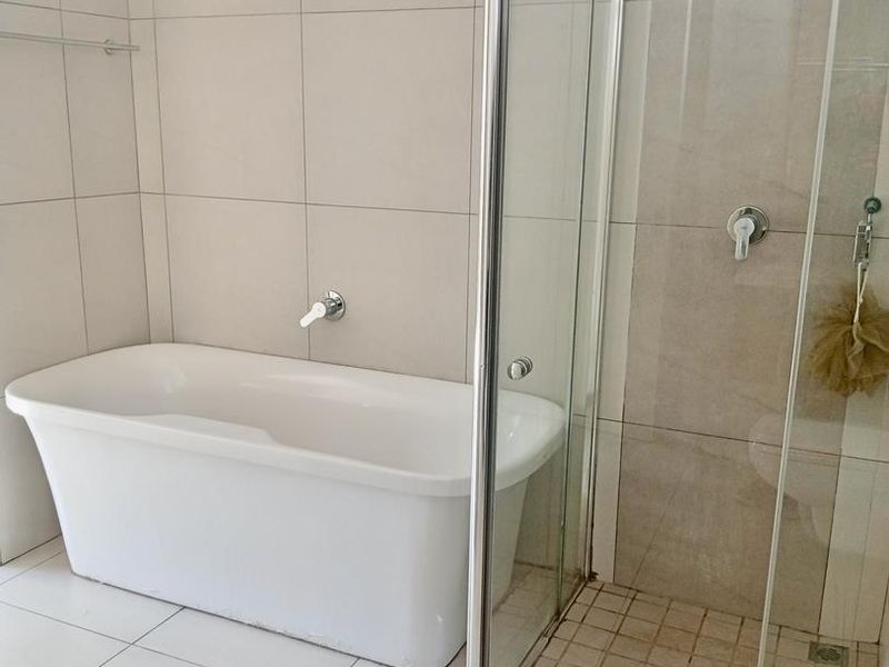 A modern bathroom featuring a white freestanding bathtub and a separate glass-enclosed shower with neutral ceramic tiling throughout.