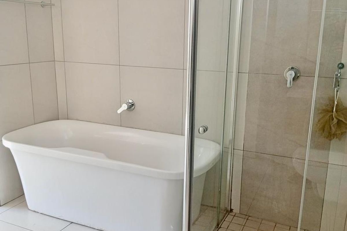 A modern bathroom featuring a white freestanding bathtub and a separate glass-enclosed shower with neutral ceramic tiling throughout.