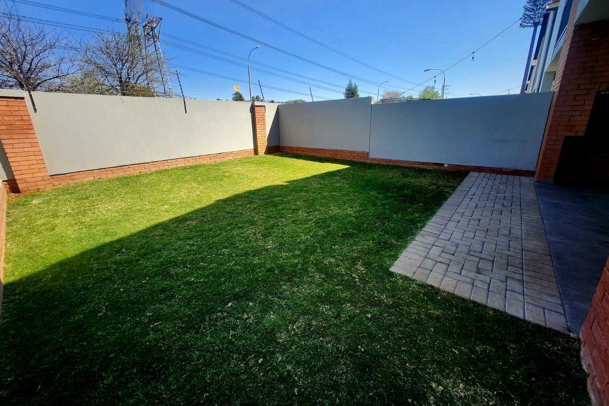 A private rear garden featuring a well-maintained lawn, paved walkway, and secure perimeter wall with electric fencing.