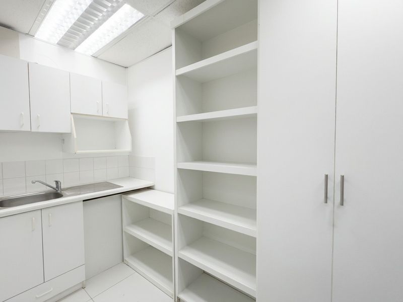 A clean and functional scullery or utility area featuring white built-in cabinetry, open shelving, and a stainless steel sink with tiled splashback.