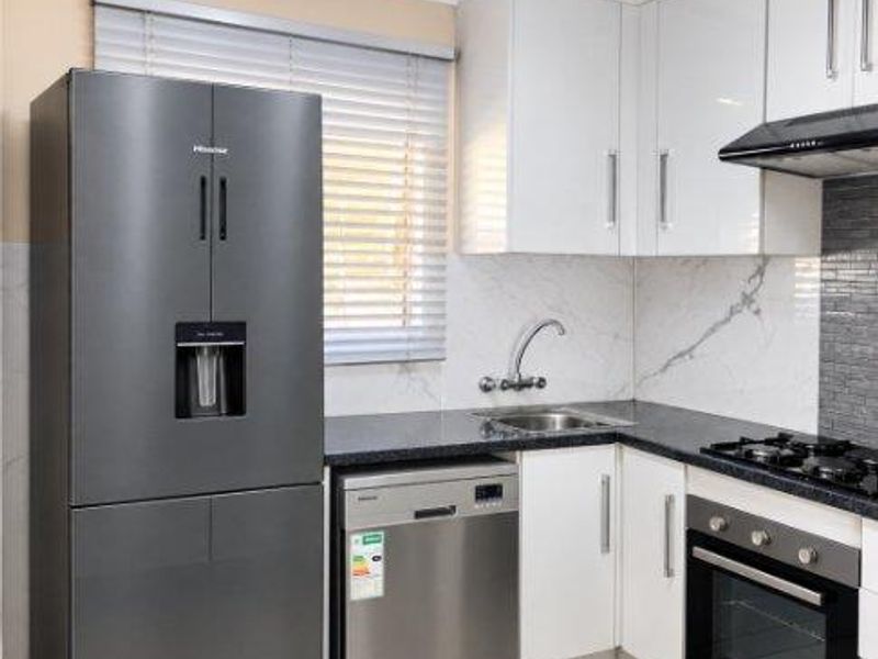 Modern kitchen featuring white cabinetry, granite countertops, built-in oven, gas hob, extractor fan, and tiled flooring.
