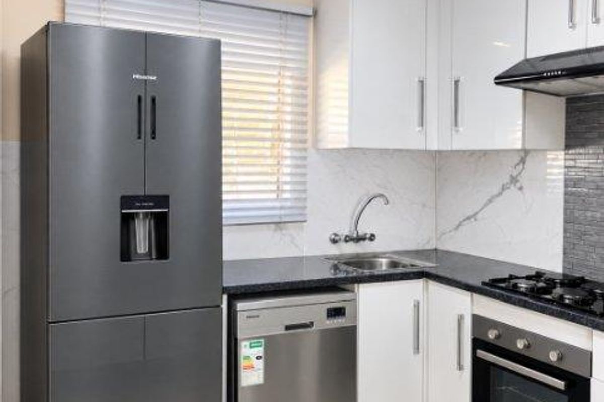 Modern kitchen featuring white cabinetry, granite countertops, built-in oven, gas hob, extractor fan, and tiled flooring.