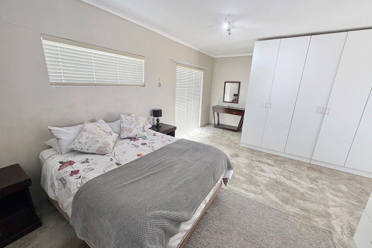 A spacious bedroom featuring neutral carpeting, built-in white wardrobes, and venetian blinds, offering a clean and functional living space.