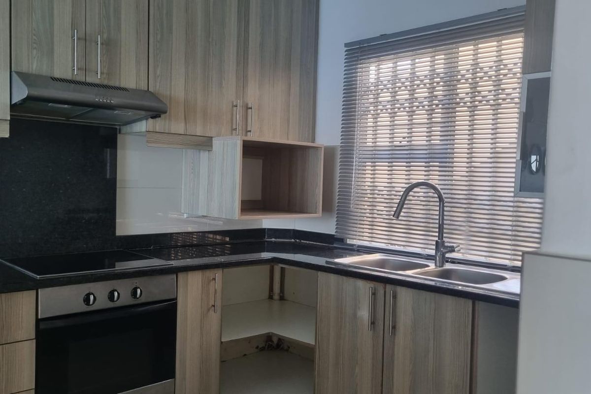 Modern kitchen featuring wood-look cabinetry, granite countertops, integrated oven and hob, and a stainless steel sink with a contemporary mixer tap.