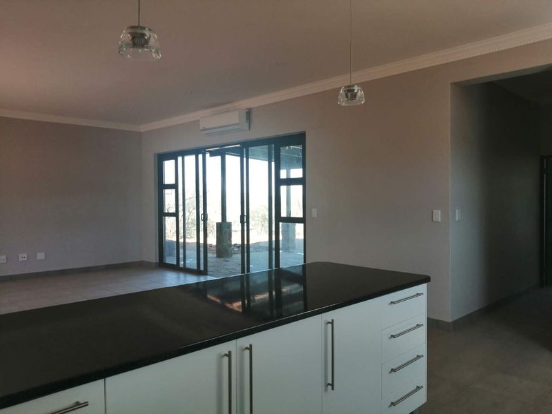 Spacious open-plan living area featuring a modern kitchen island with granite countertops, tiled floors, and large sliding doors leading to an outdoor patio.