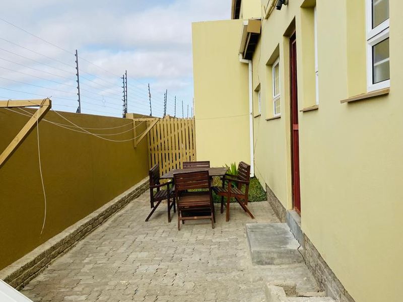 A rear exterior view of the apartment featuring a paved patio area, enclosed by a timber fence and secured with electric fencing.