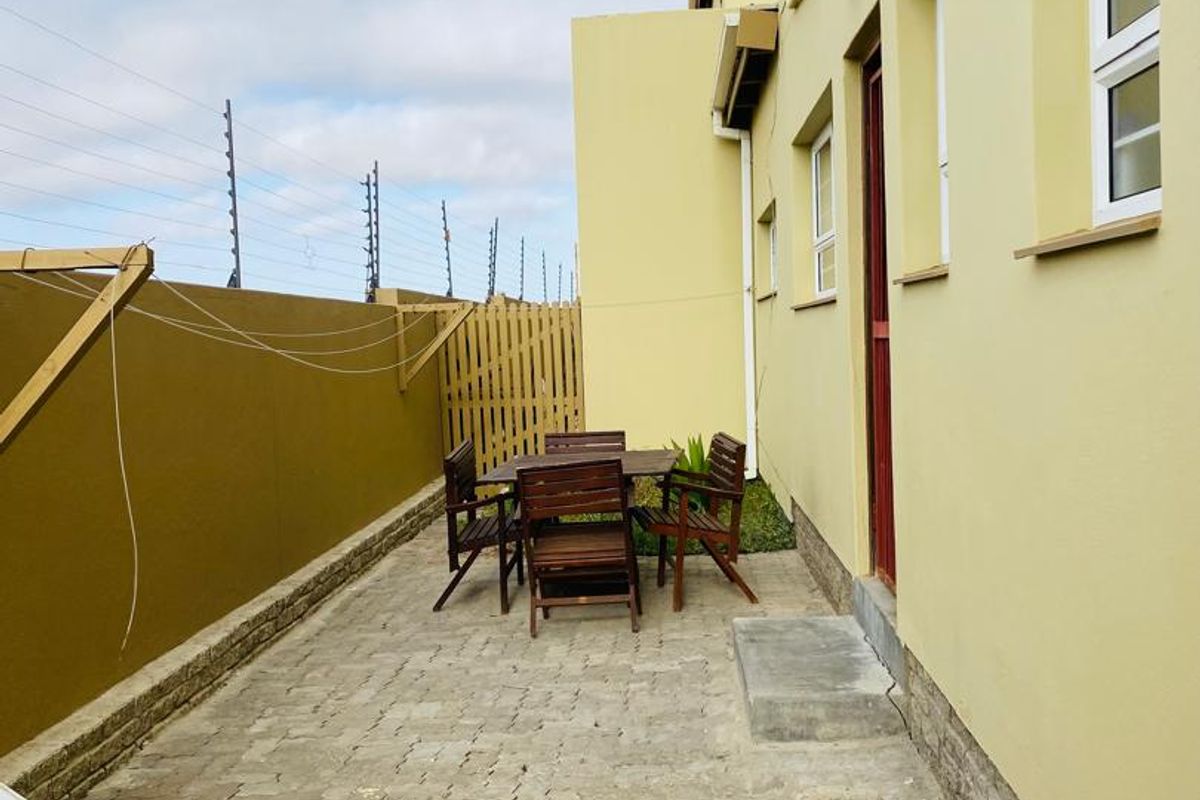 A rear exterior view of the apartment featuring a paved patio area, enclosed by a timber fence and secured with electric fencing.