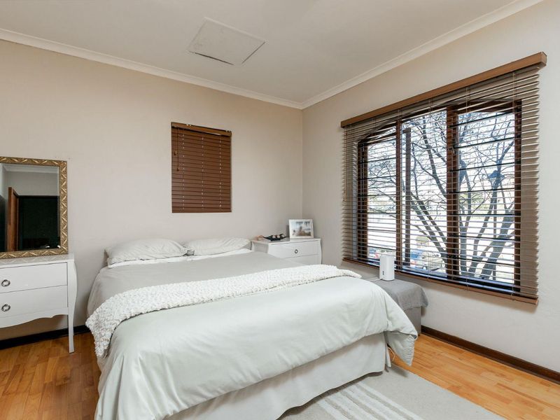 A well-lit bedroom featuring laminate flooring, neutral wall tones, and venetian blinds on the windows.