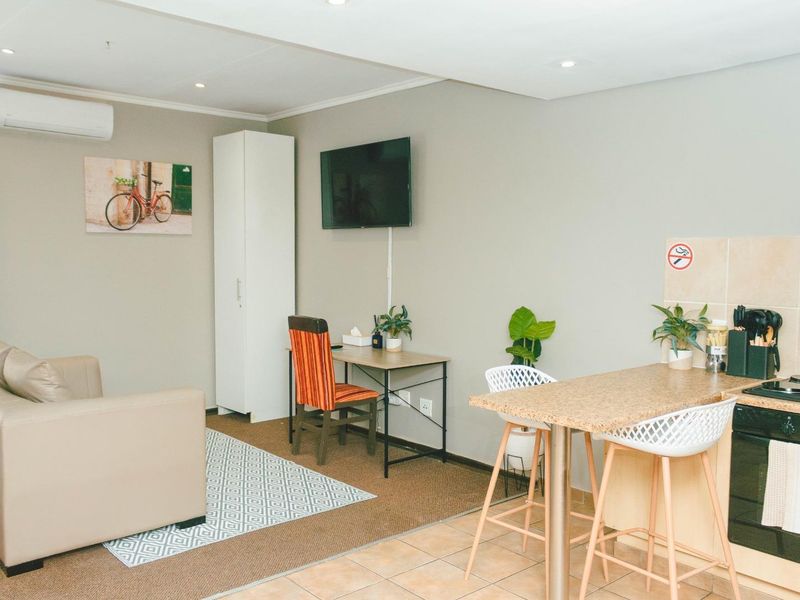 Open-plan living area featuring a compact kitchen with built-in oven and hob, adjacent to a carpeted lounge space with air conditioning.