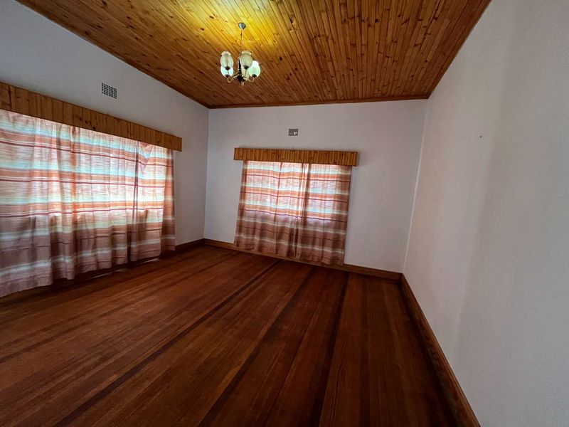 An empty bedroom featuring polished hardwood flooring and a traditional timber-clad ceiling with a central light fixture.