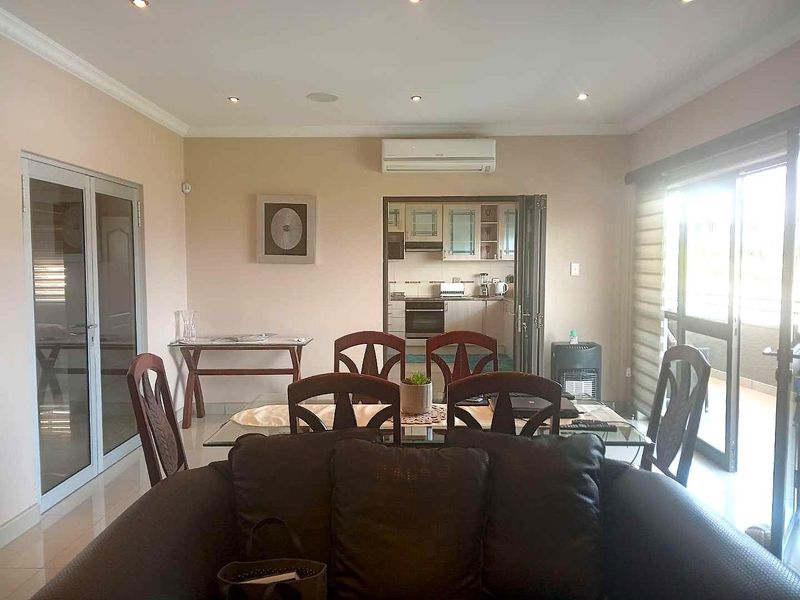 Open-plan living and dining area featuring tiled floors, recessed lighting, and a split-system air conditioner, with direct access to an adjoining kitchen and balcony.