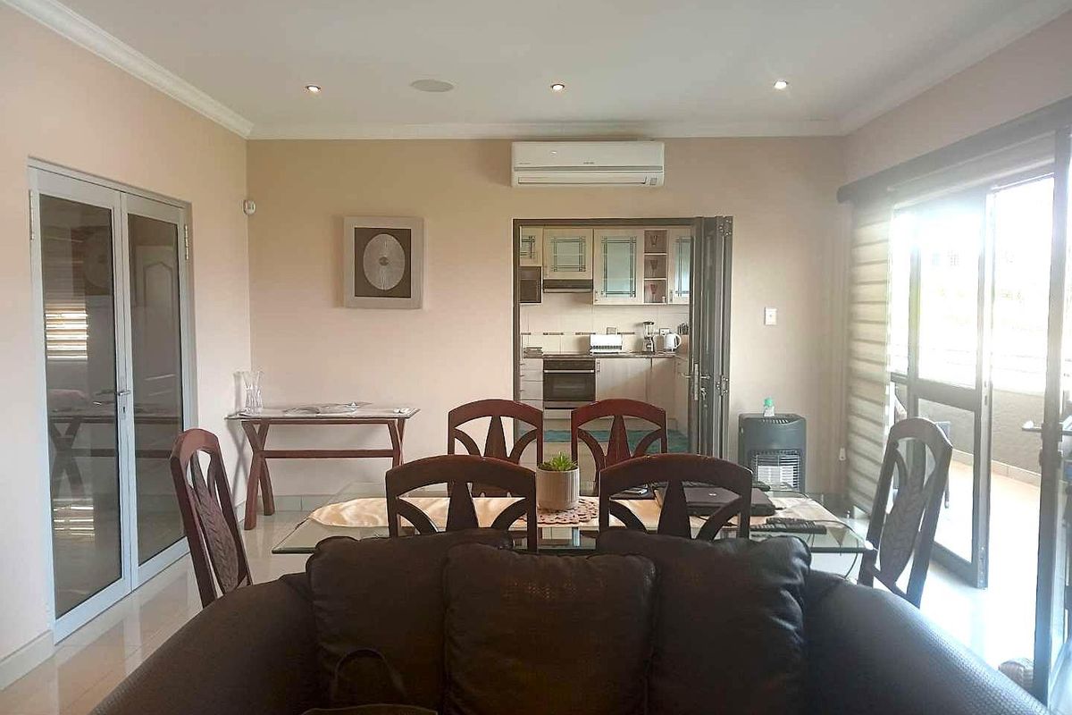 Open-plan living and dining area featuring tiled floors, recessed lighting, and a split-system air conditioner, with direct access to an adjoining kitchen and balcony.