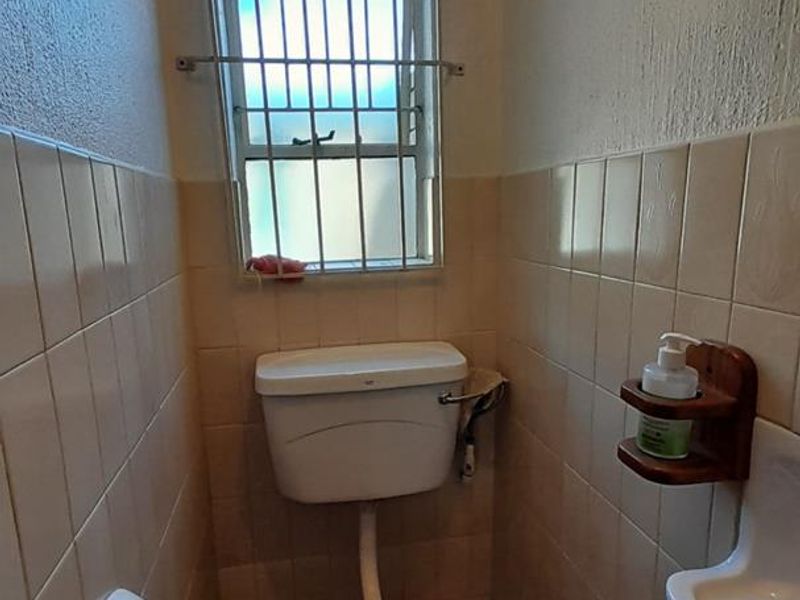 A compact guest bathroom featuring a standard toilet, wall-mounted basin, and neutral ceramic tiling with security bars on the window.