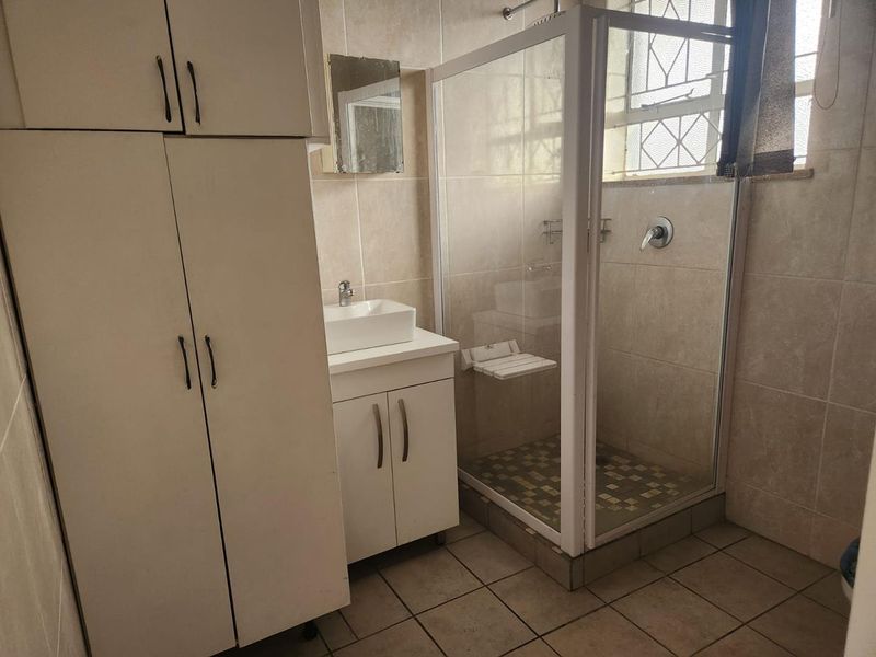 A functional bathroom featuring a shower enclosure, vanity with vessel sink, and ample built-in storage cabinetry with neutral wall and floor tiling.