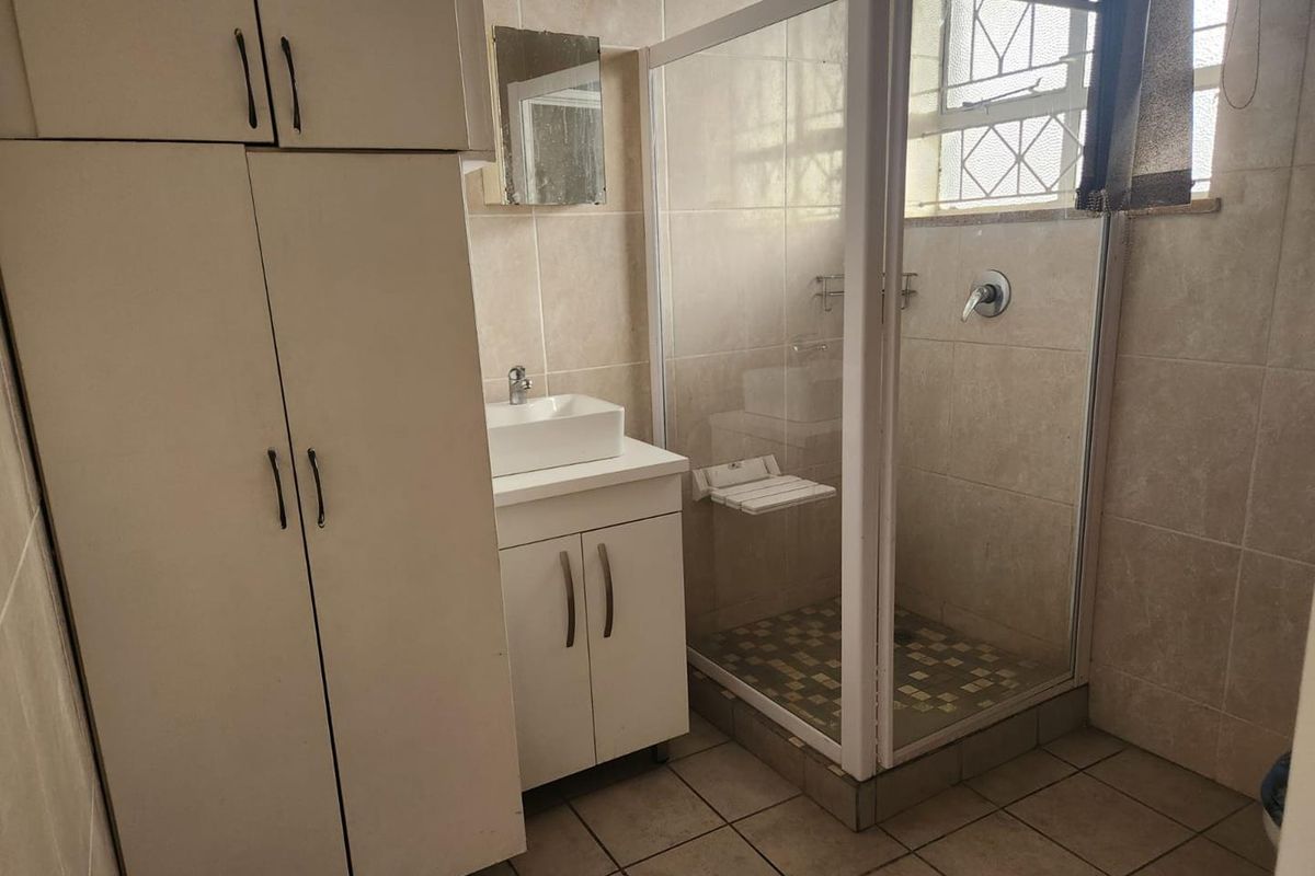 A functional bathroom featuring a shower enclosure, vanity with vessel sink, and ample built-in storage cabinetry with neutral wall and floor tiling.