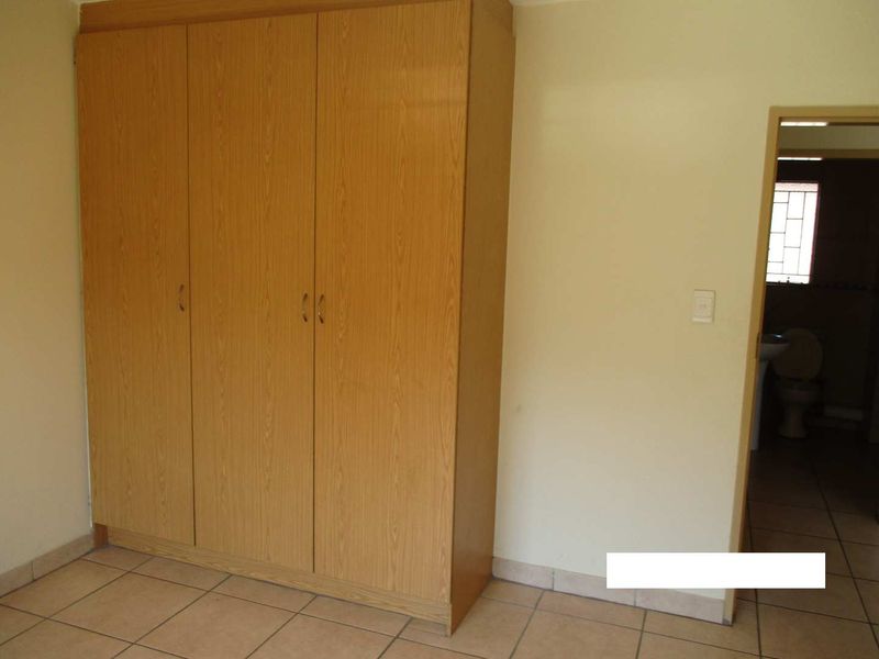 A bedroom featuring built-in wooden wardrobes and tiled flooring, with an adjacent view into a bathroom area.