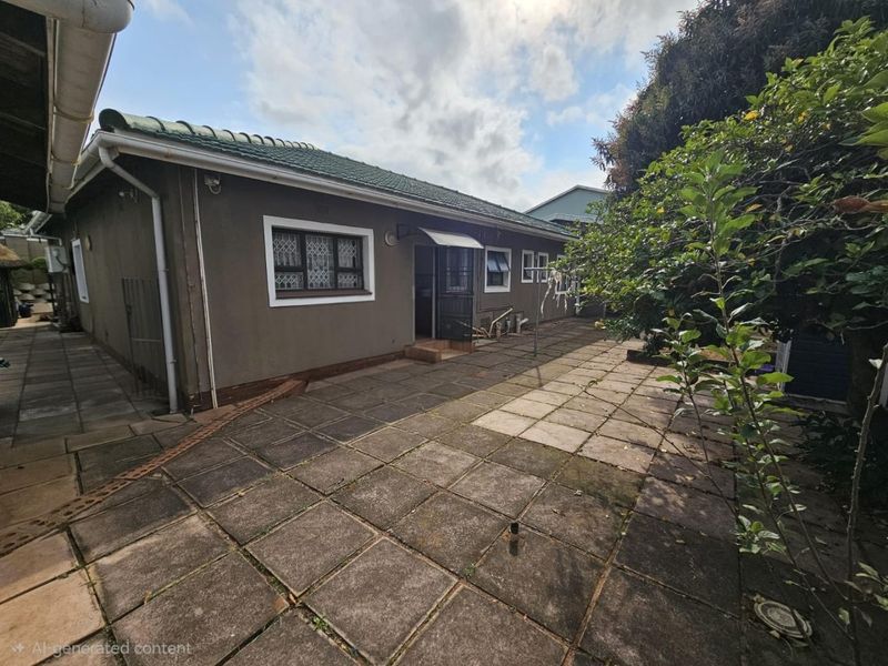 Rear exterior view of the house featuring a paved patio area, tiled roof, and security features on windows and doors.