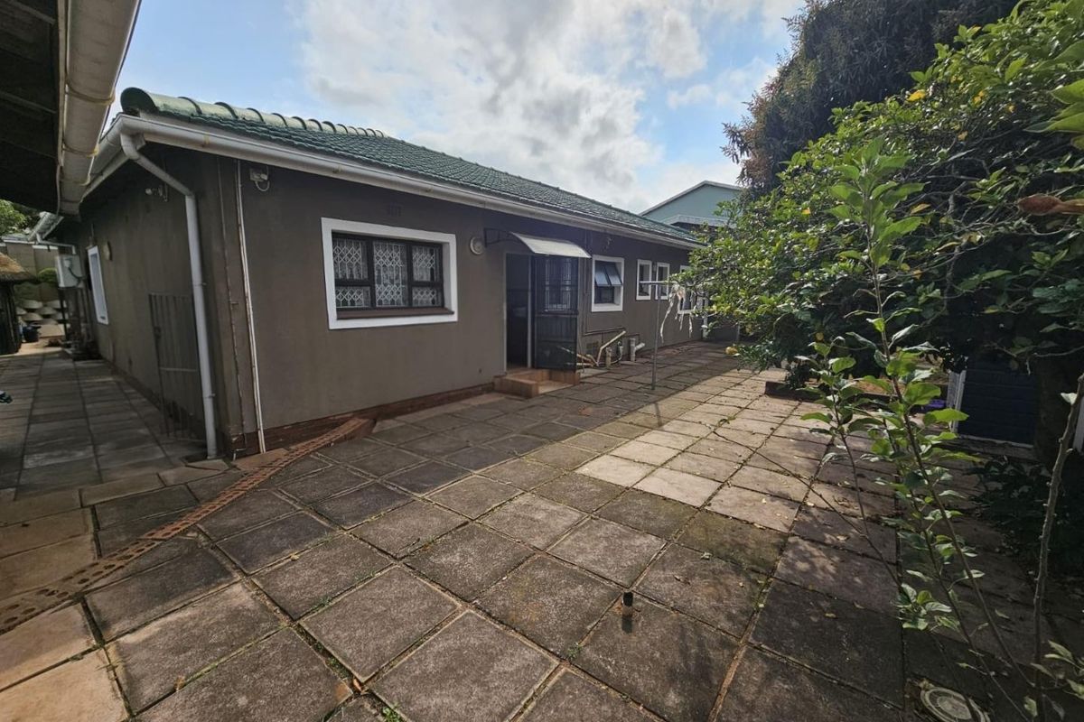 Rear exterior view of the house featuring a paved patio area, tiled roof, and security features on windows and doors.