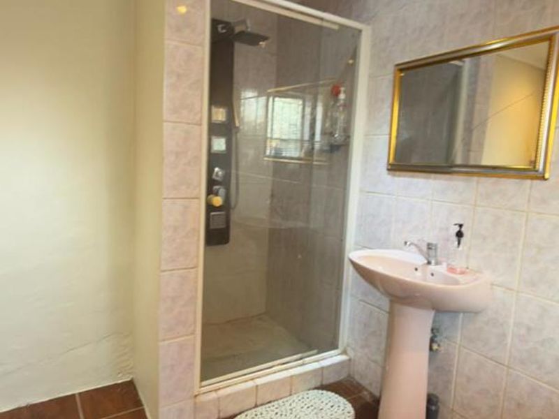 A functional bathroom featuring a pedestal basin, a glass-enclosed shower, and tiled finishes throughout, offering a clean and practical space.