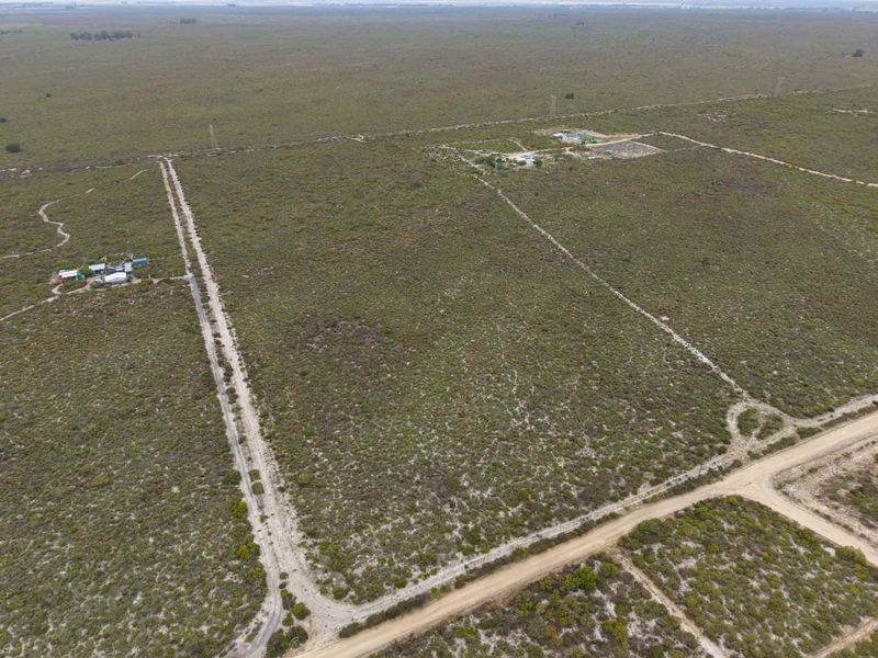 An aerial view of a large expanse of agricultural land featuring dirt access roads, perimeter fencing, and small existing outbuildings.