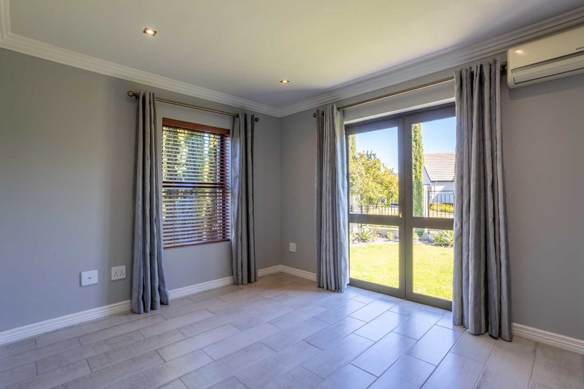 A bright, empty bedroom featuring tiled flooring, recessed lighting, and a split-system air conditioner, with direct access to the garden through glass doors.