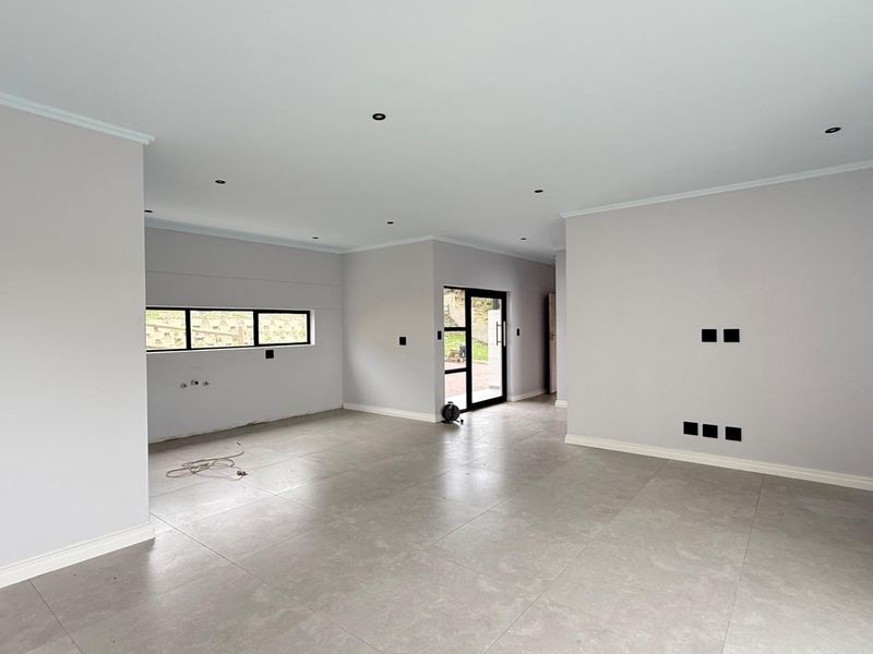 A spacious, modern open-plan living area featuring neutral grey floor tiles, recessed lighting, and clean finishes, ready for custom interior design.